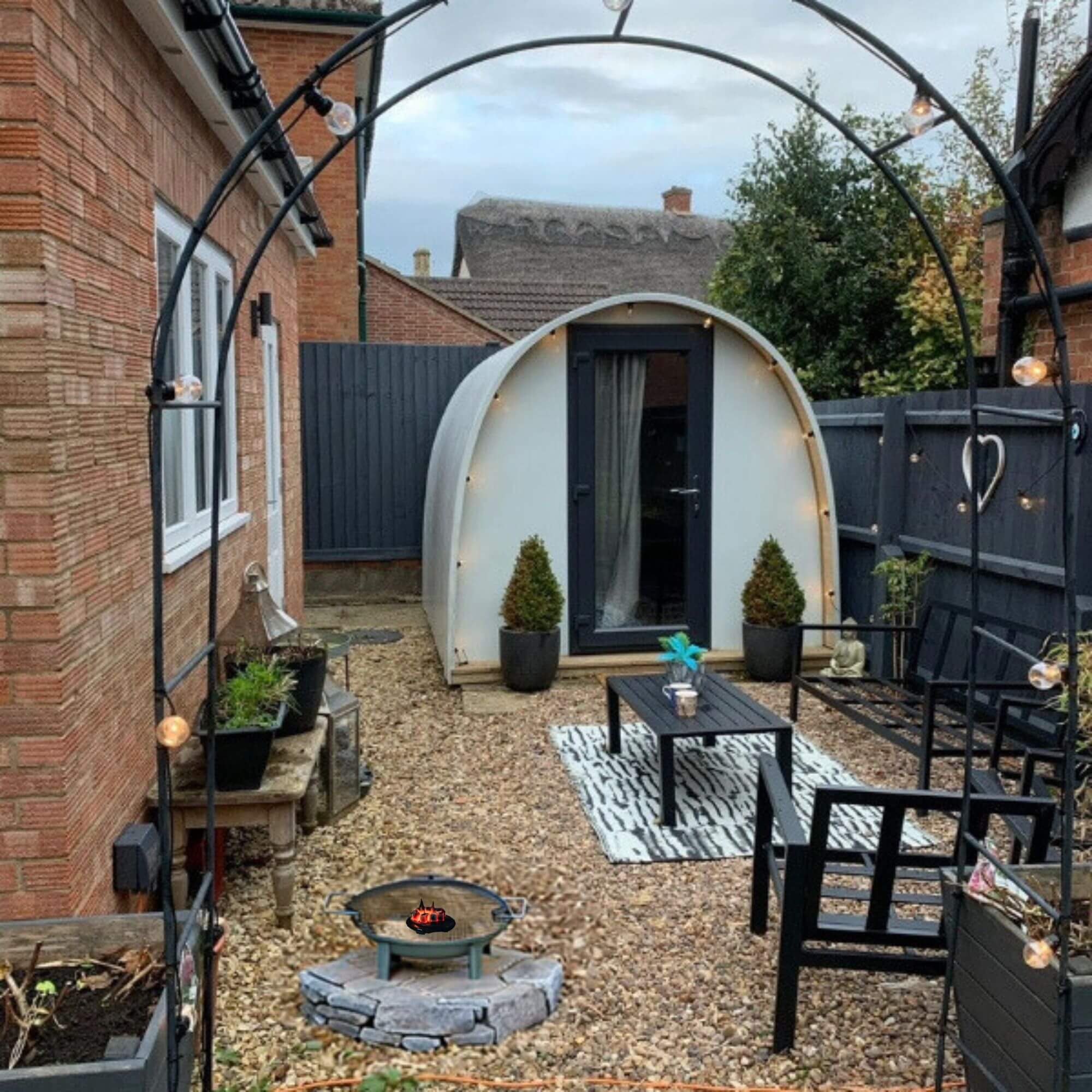 Image of white garden Pod in winter with lush foliage and fire pit